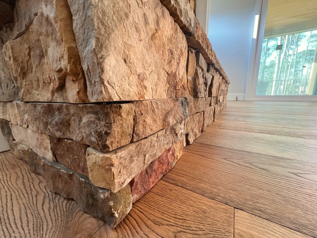 Precision hand-scribed wide plank hardwood meeting stacked stone hearth by CRG Flooring